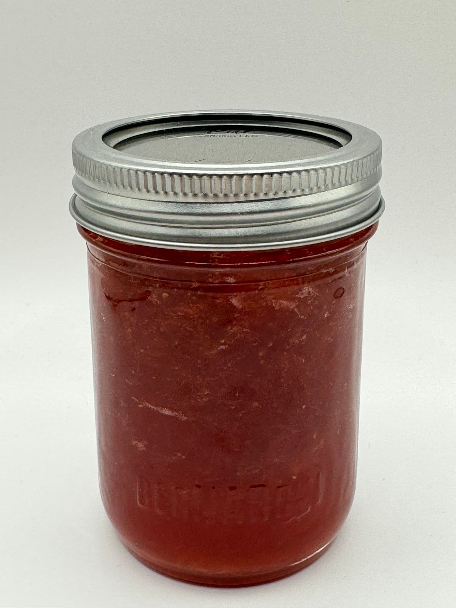 A glass jar filled with a reddish substance and topped with a silver metal lid.