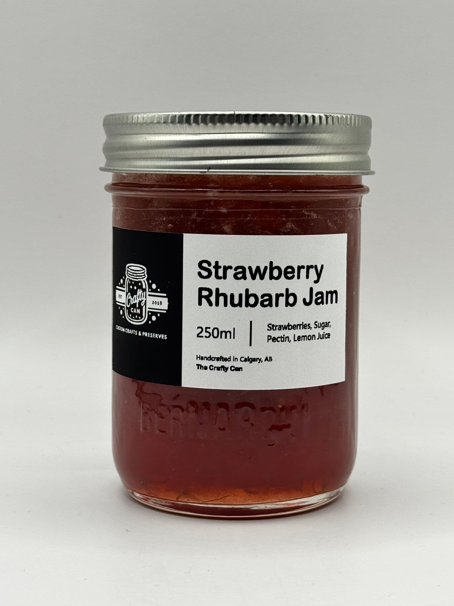 A jar of strawberry rhubarb jam with a silver lid and a white label displaying the contents and volume.
