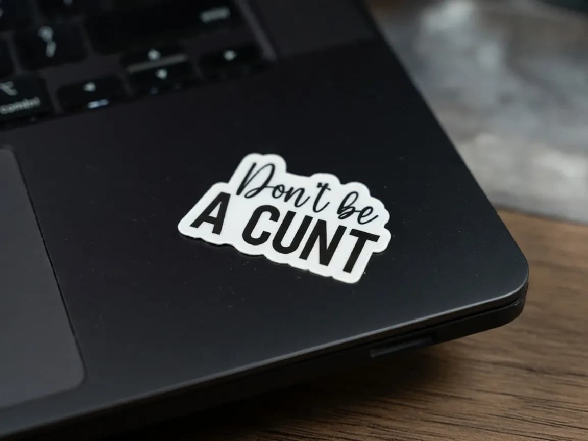 A white sticker with black text reading "Don't be A CUNT" is placed on a black laptop surface.